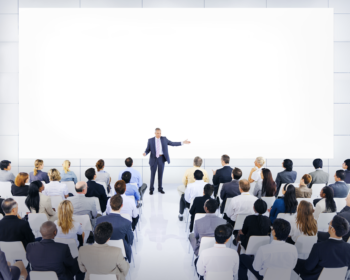 uomo che parla ad un pubblico numeroso in un'aula