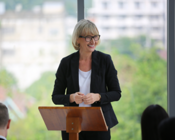 Donna al leggio che legge ad alta voce interagendo col pubblico