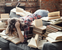 ragazza che legge piegata in avanti su divano circondata dai libri