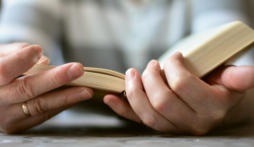 Mani di un lettore che apre un libro durante un esercizio di lettura ad alta voce.