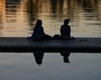 immagine di due donne sedute su un pontile riflesse nell'acqua che conversano